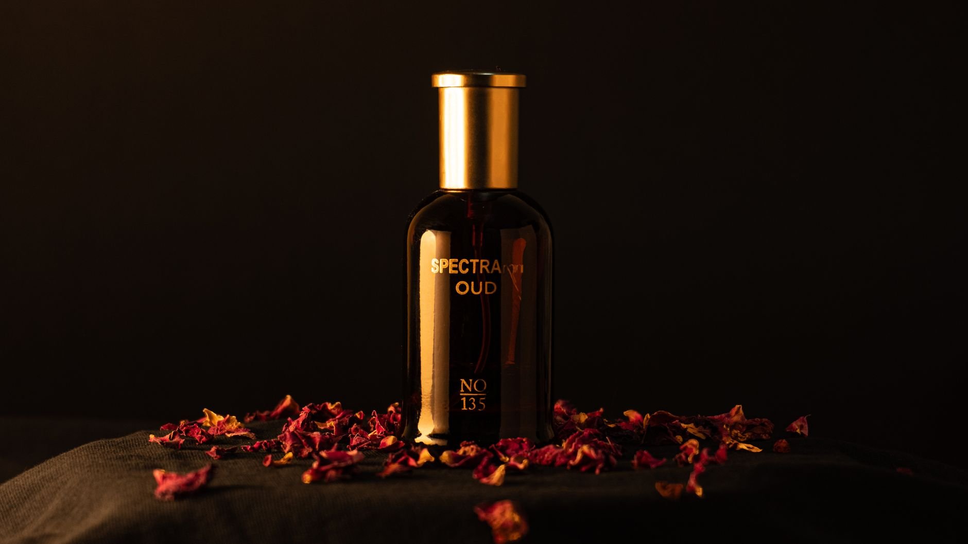 Elegant oud perfume bottle surrounded by rose petals on a dark backdrop, exuding luxury.